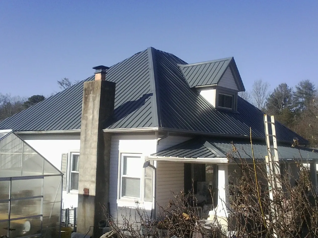 Dark blue standing seam metal roof on a white farmhouse with dormer — Slate & Tile Roof Repair by Roofing Brothers in New Lexington