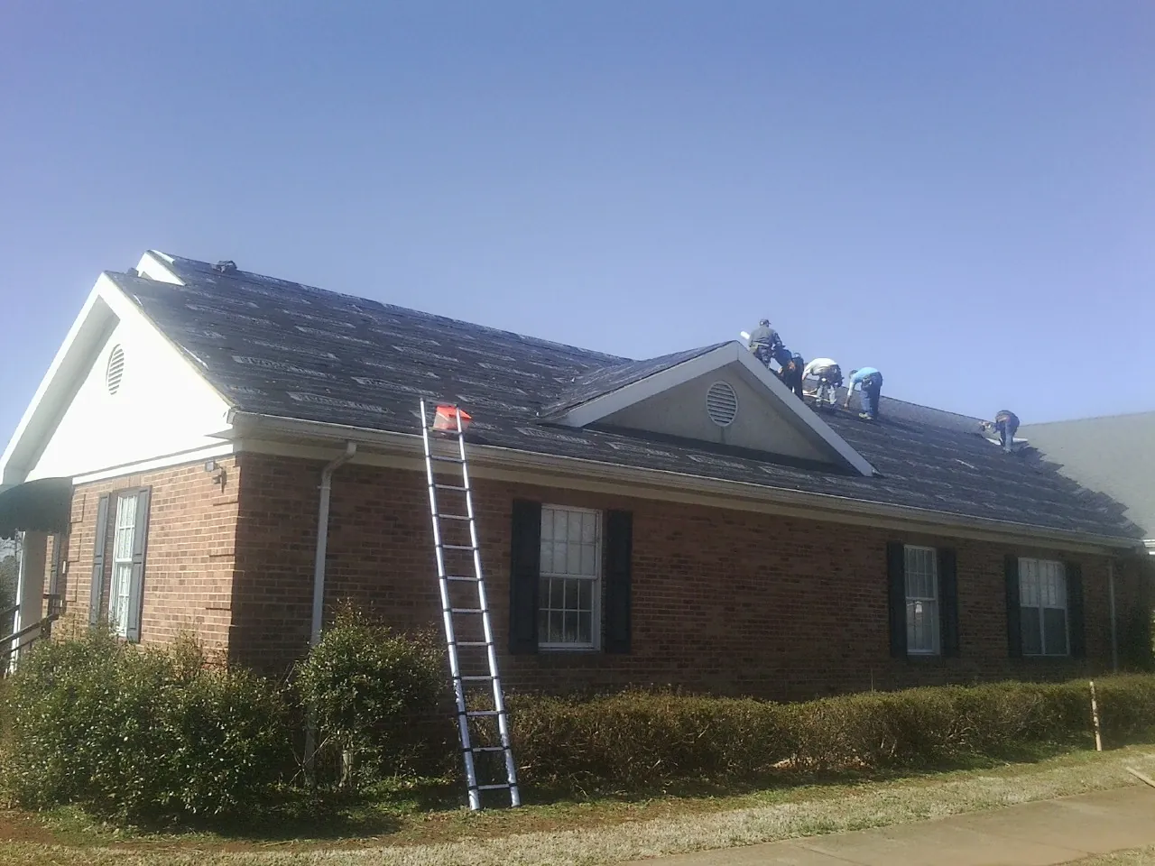 Crew tearing shingles off a brick ranch roof with a ladder set — Emergency Roof Repair work by our crew in New Lexington