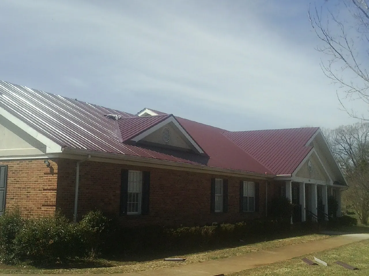 Red metal roof with gabled entries on a long brick building, from a Hail Damage Roof Repair job in New Lexington