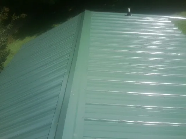 New green metal panels meeting at the ridge of a roof — Flat Roof Repair work by our crew in New Lexington