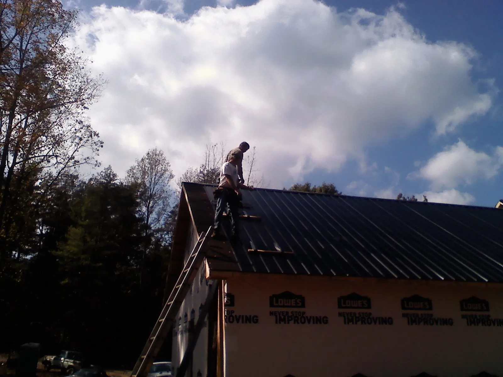 Roofer fastening dark metal panels high against a cloudy sky, from a Roof Inspection job in New Lexington