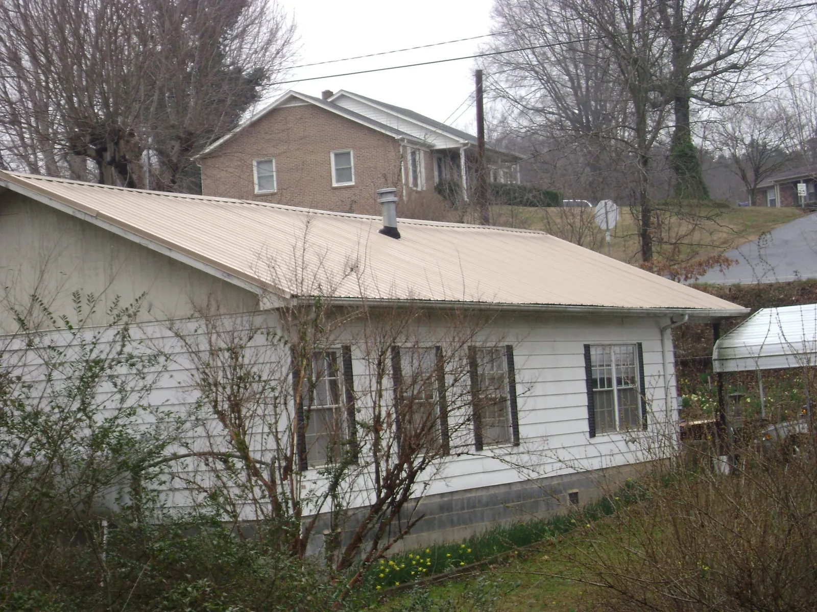 Tan metal roof on a white sided house set into a hillside — Commercial Roofing by Roofing Brothers in New Lexington